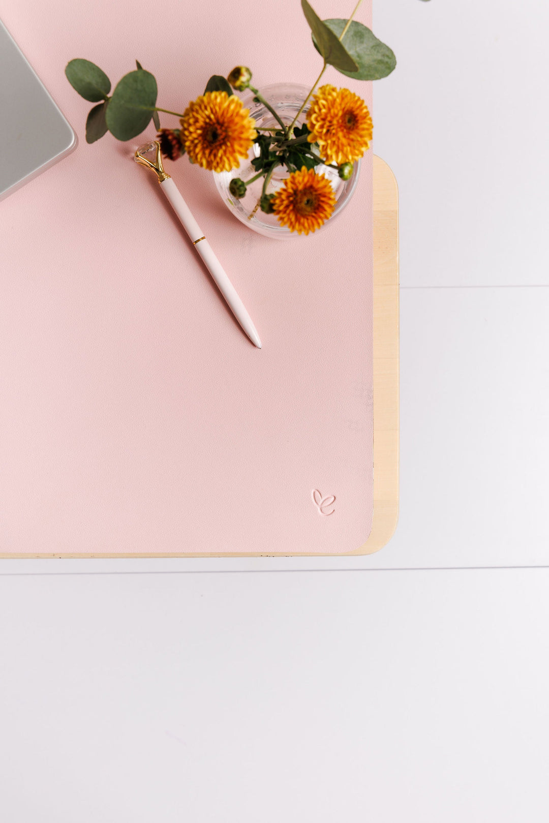 Blush vegan leather desk mat styled with elegant flowers and pens, showcasing its smooth surface and refined aesthetic for workspace decor.