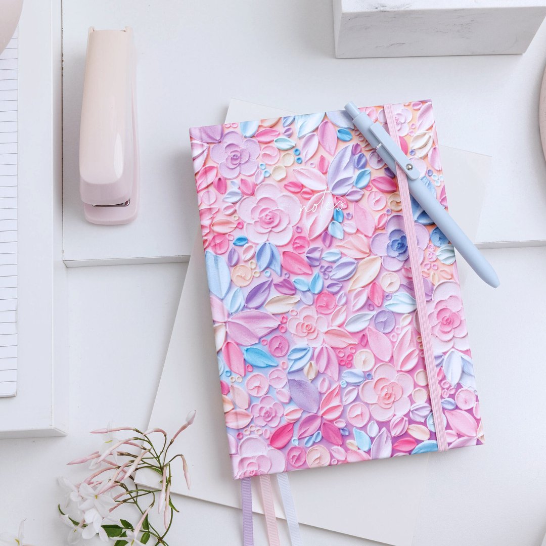 Aurora A5 notebook with pink, floral design by Amy Lockwood, with elastic closure, ribbon bookmarks, and a pen.