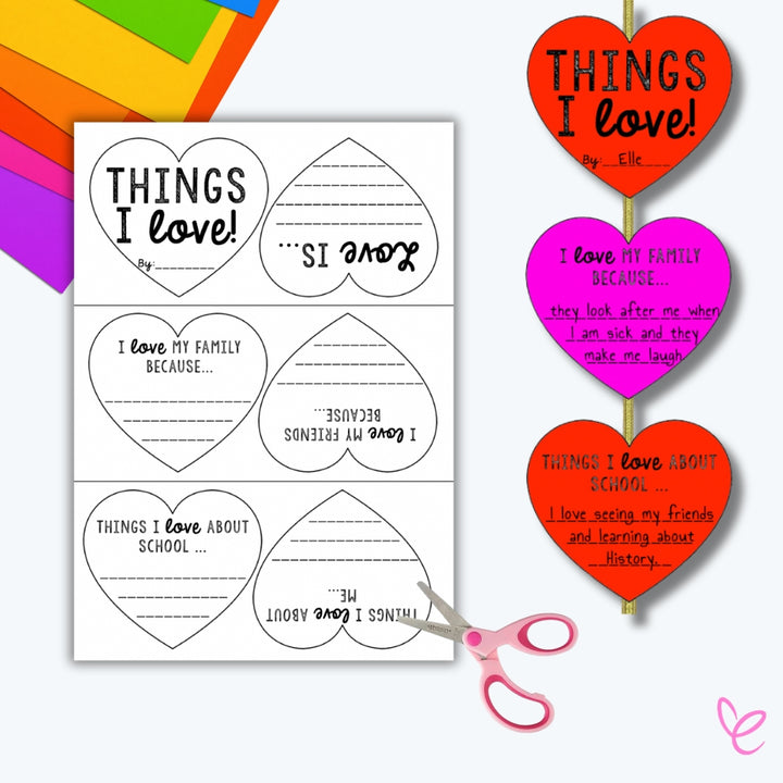 A completed "Things I Love" heart writing craft, showing a cut-out, colored, and assembled heart-shaped hanging decoration with handwritten responses. Surrounding materials include scissors and colourful paper.