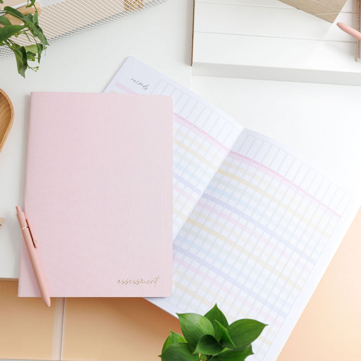 Styled photo of the blush assessment journal, with one closed on top of an open bright spread, surrounded by decorative objects.