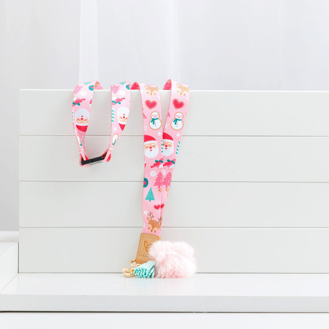 Pastel pink Christmas lanyard with festive prints, pom-pom, tassel, gold clasp, 'Mrs Edgar' patch, and breakaway clasp, resting over a box.