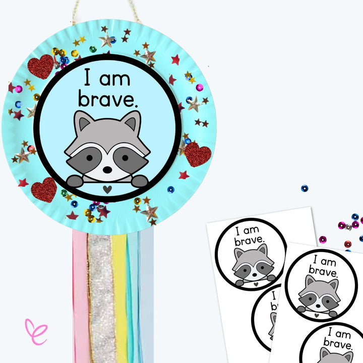 A blue version of the "I am brave" craft featuring a raccoon illustration. The craft is decorated with stars, beads, and heart stickers, with colourful ribbons hanging below. Printable templates are included in the background.