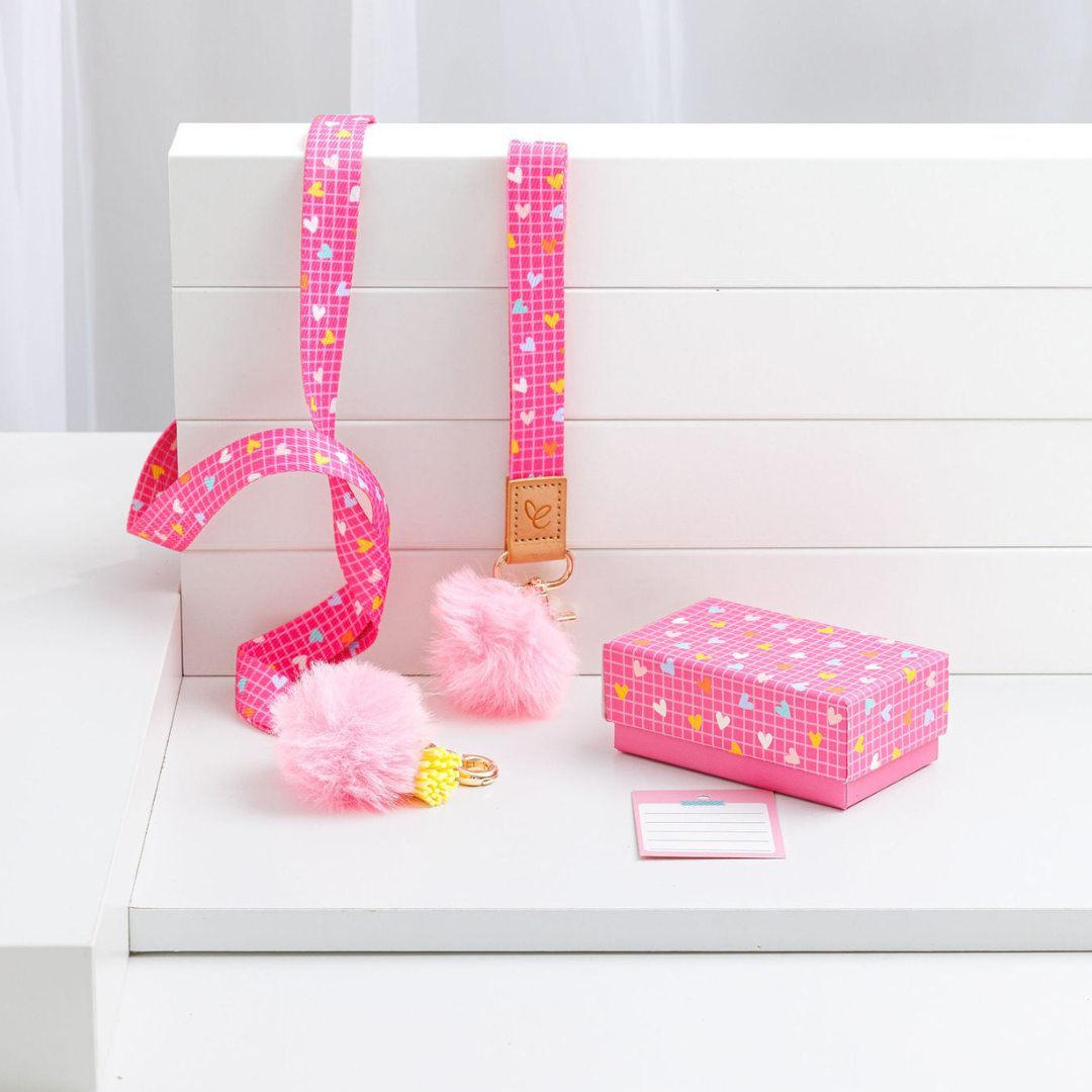 Bright pink lanyard and matching wristlet with a white grid and heart pattern, featuring a light pink pom-pom, yellow tassel, and gold swivel clasp. Comes with a matching bright pink gift box and thank-you card for teachers.