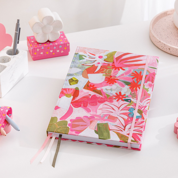 2025 Classic Weekly Teacher Planner named Postcards on a desk, showcasing bright floral art in pinks, greens, and blues.