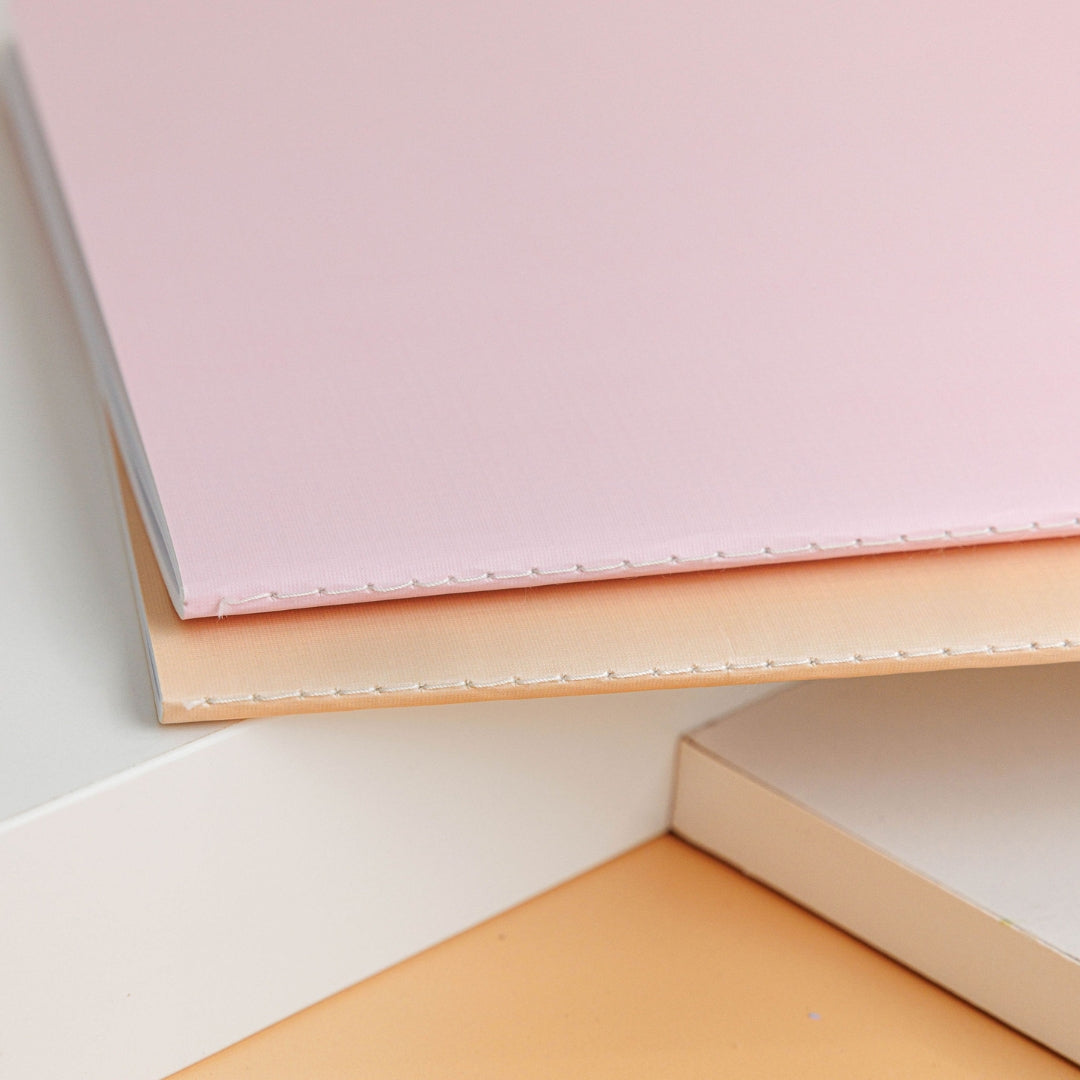 Blush journal placed on a tan assessment journal, showcasing the fine stitching and luxurious design.