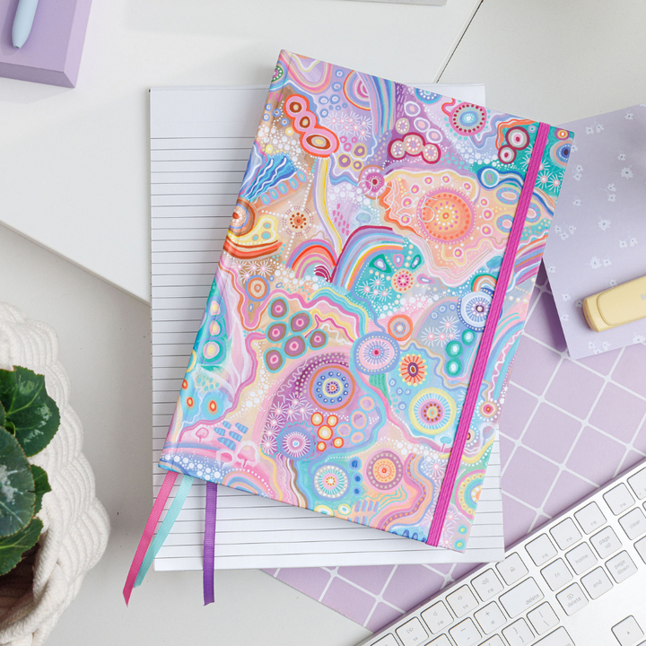 Purple, personal planner featuring Aboriginal art by Jagun-Country, resting on a lined notebook on a desk, showcasing vibrant, detailed patterns.