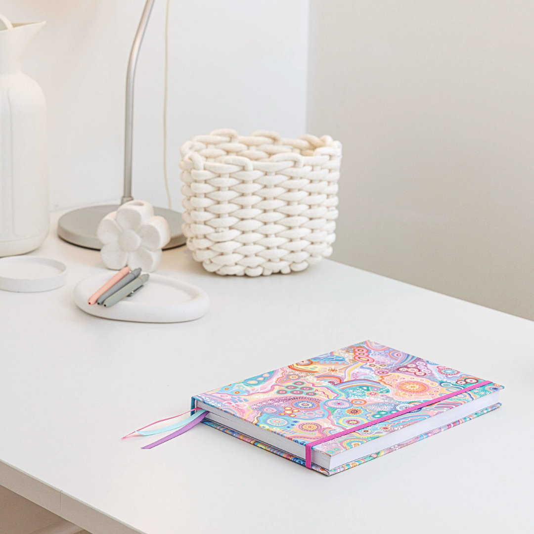 Zoomed-out view of the personal planner featuring Jagun-Country Aboriginal art on the cover and a purple enclosure, sitting on a desk with stationery in the background.