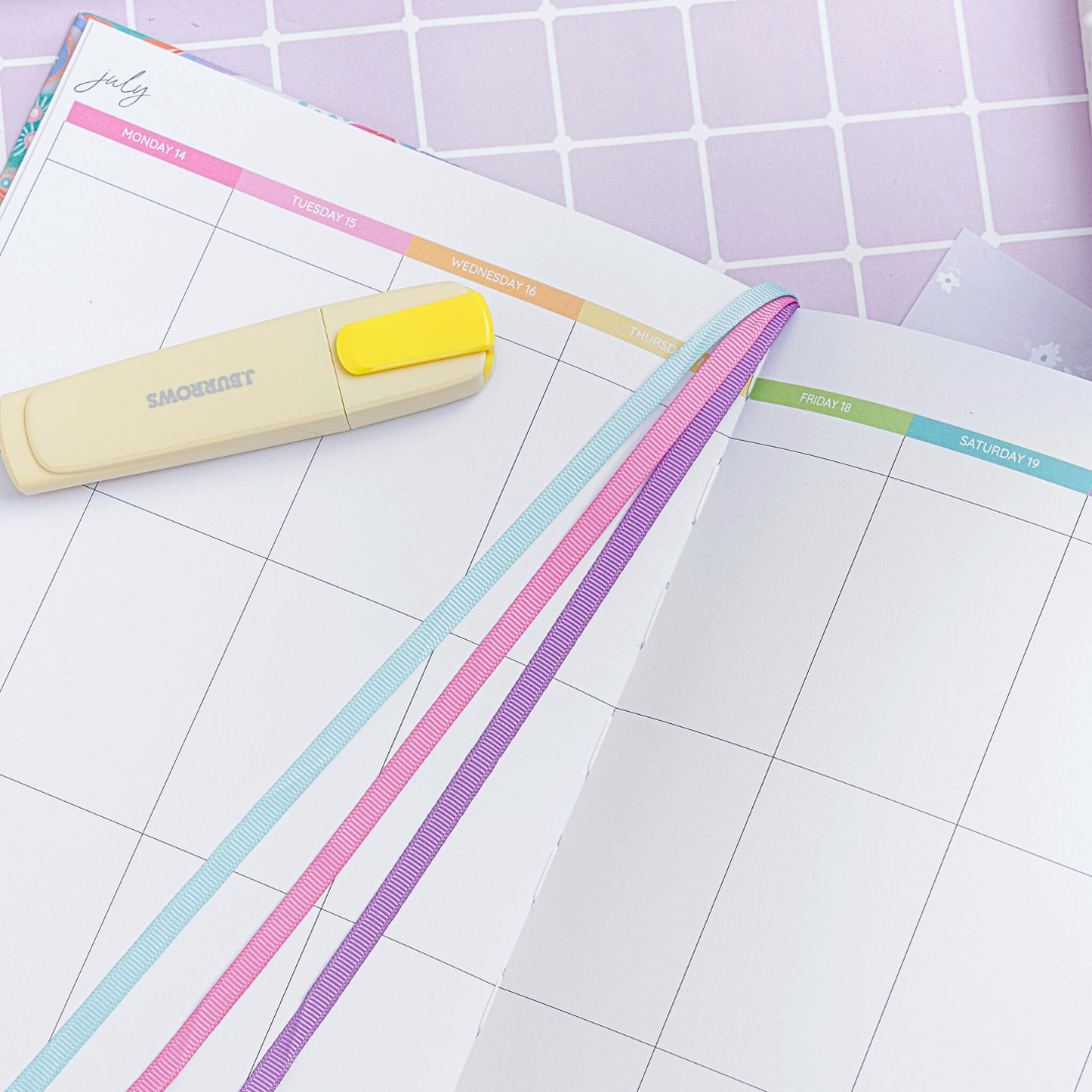 Close-up of the top of the open weekly planner showing the July calendar, with a yellow highlighter and ribbon dividers resting on the page.