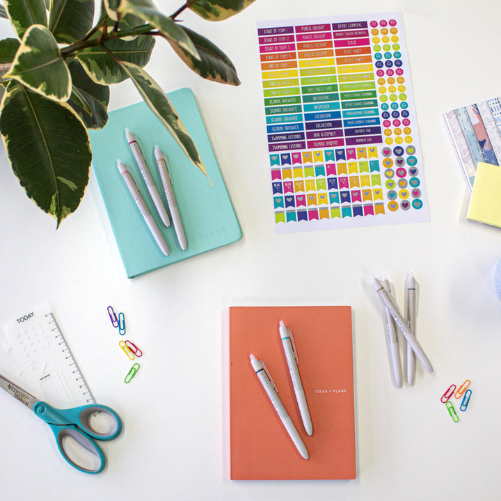 Waai ballpoint pens with erasable ink displayed on top of books, surrounded by stickers and various stationery items for a creative workspace.