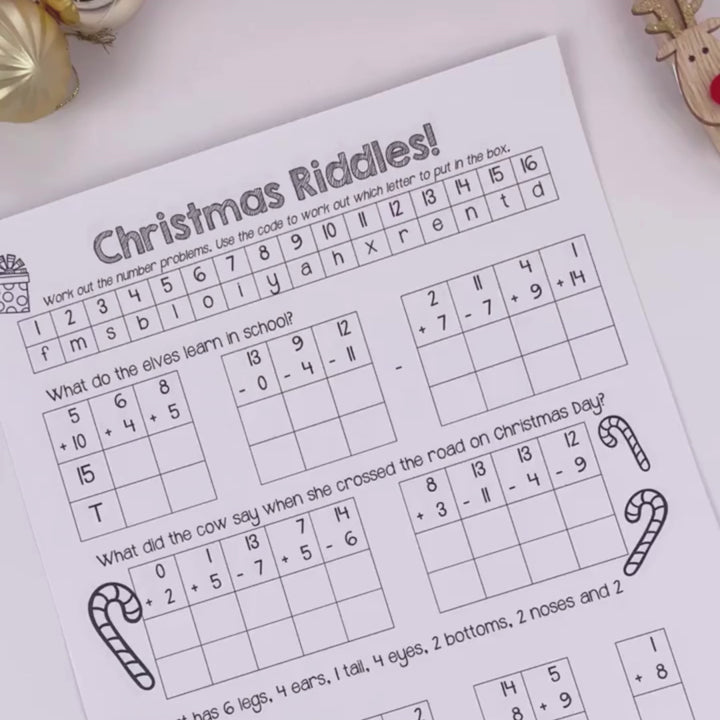 A video of a women showcasing the Christmas Crack the Code Riddles digital teacher download displayed on a desk with festive decorations, including ornaments and holiday accents.