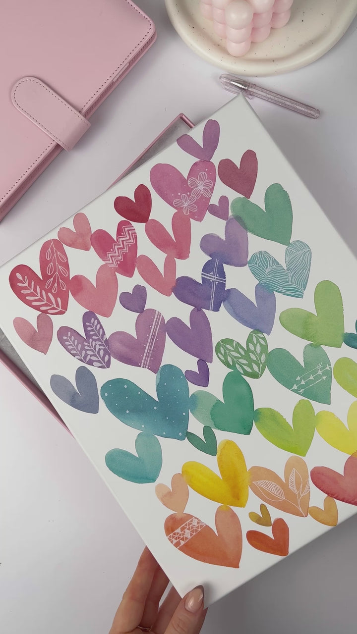 Woman showcasing the 'Watercolour Hearts' 2025 Signature Weekly Brights teacher planner, highlighting vibrant internals and cover design.